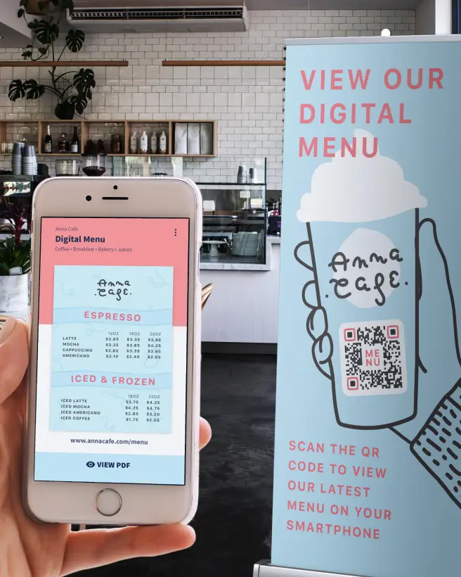 Hand holding an iPhone displaying a menu that was scanned from the QR Code on the cafe's banner in the background.