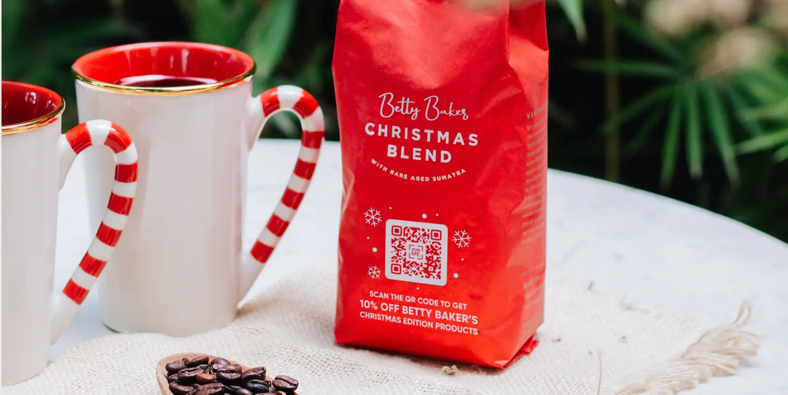 Two coffee cups and a red package of Christmas Blend coffee on a tabletop.