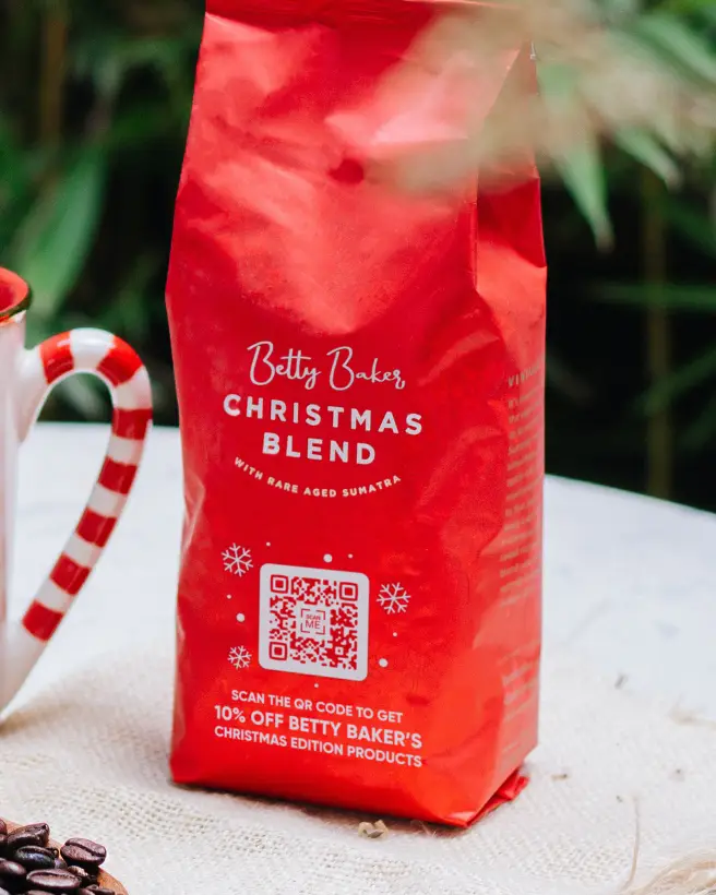 Coffee cup handle and a red package of Christmas Blend coffee on a tabletop.