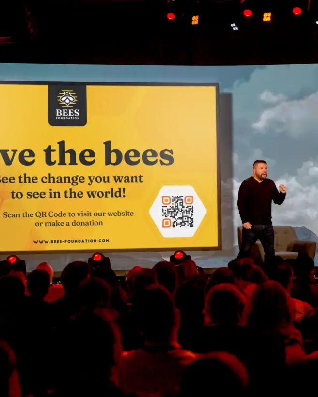 A man giving a presentation at a nonprofit event. A QR Code for donations is on screen.