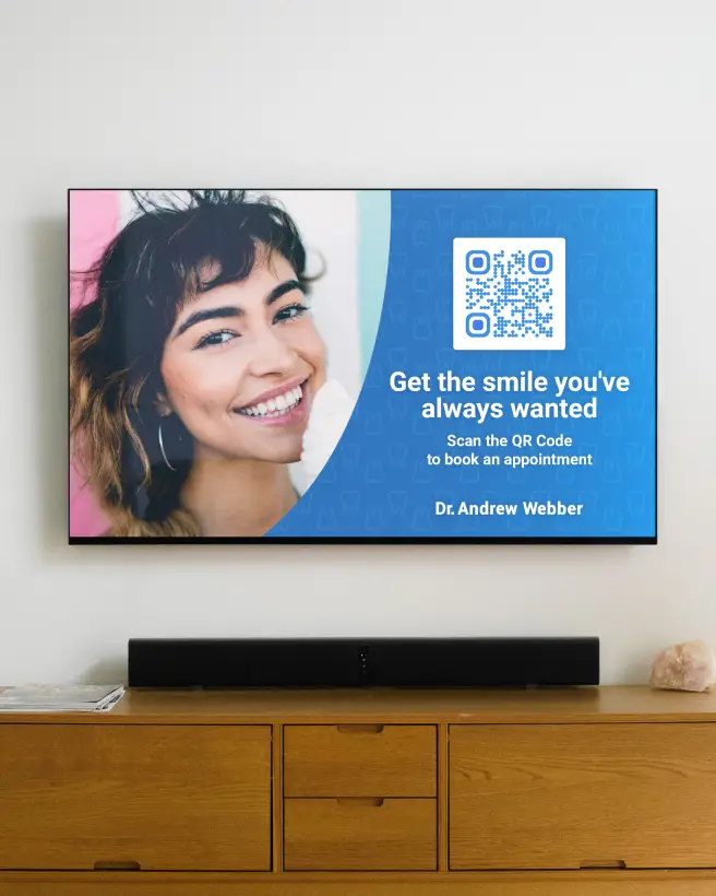 A TV on a wall with a dentists's ad showing a woman smiling and a QR Code that can be scanned to book an appointment. There's a table below the TV with a sound bar on it.