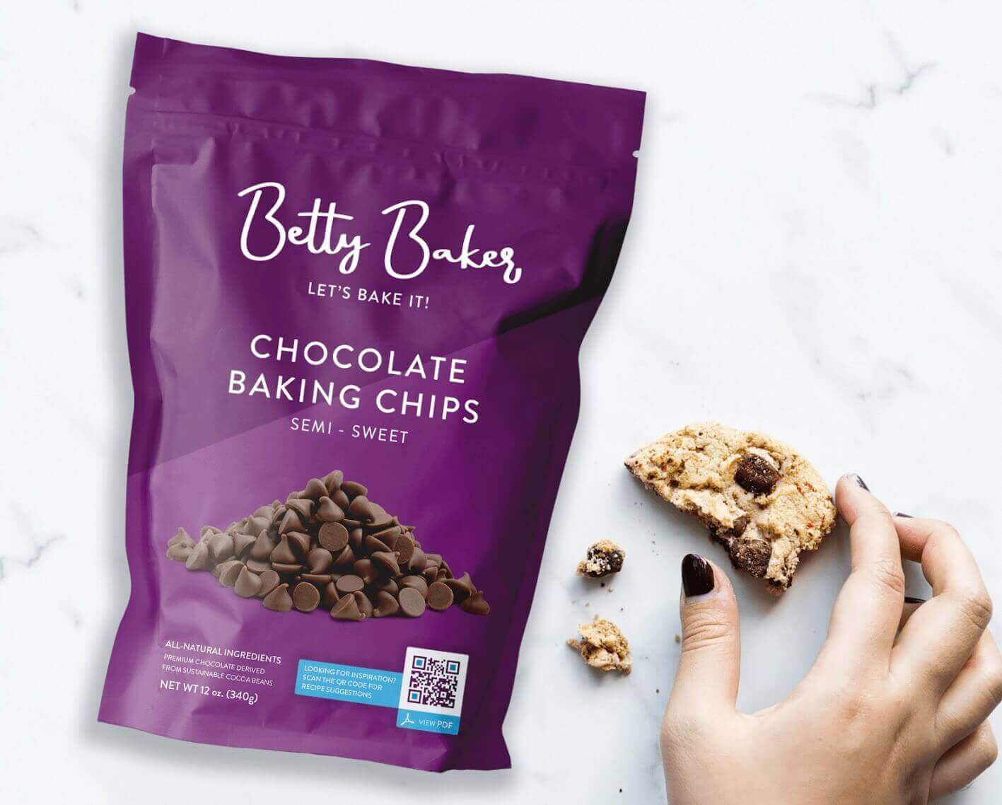 A hand holding a half-eaten cookie next to purple packaging that displays chocolate chips and a QR Code on it