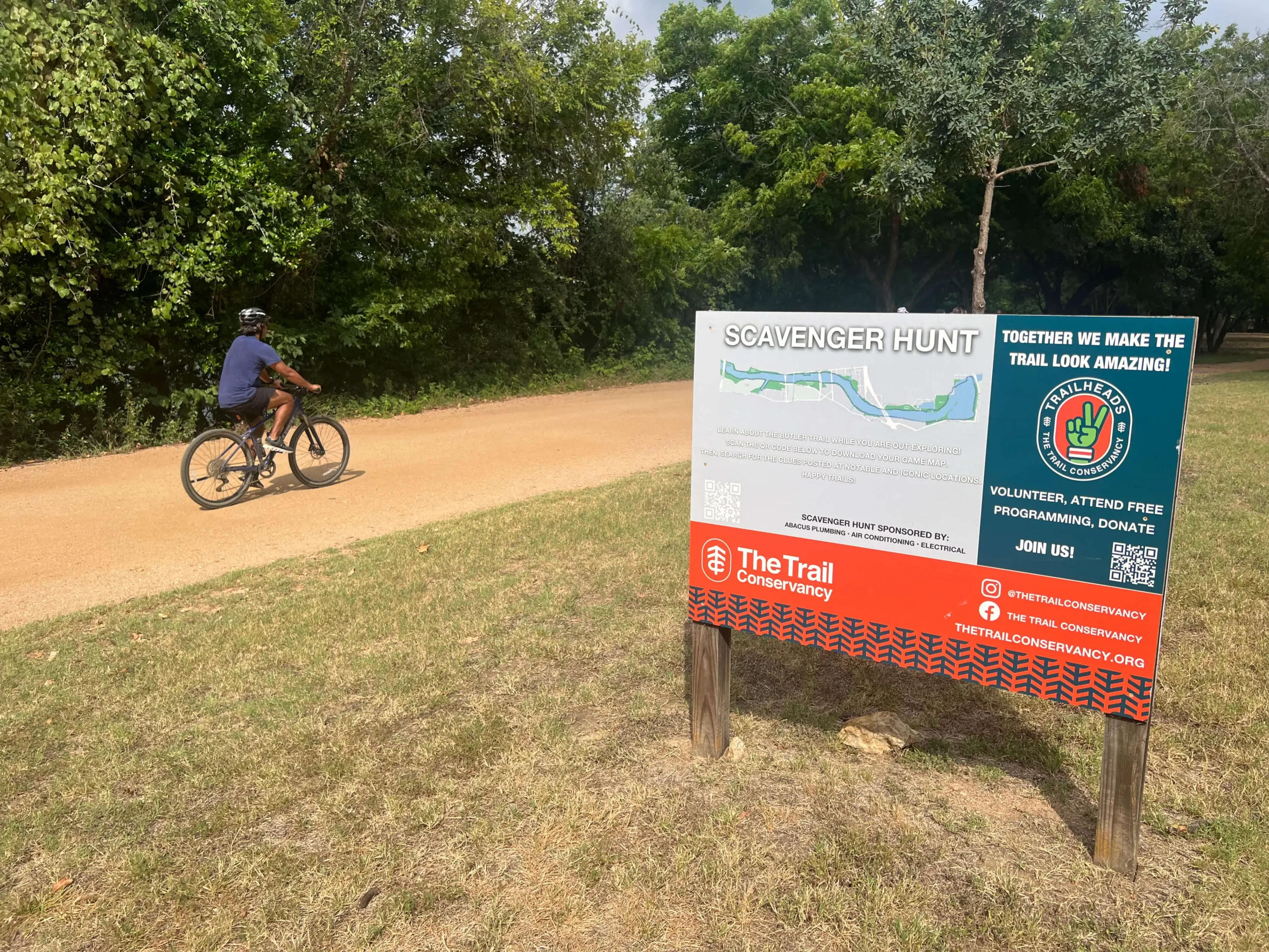 Park cyclist riding past a scavenger hunt sign with a Bitly QR Code.